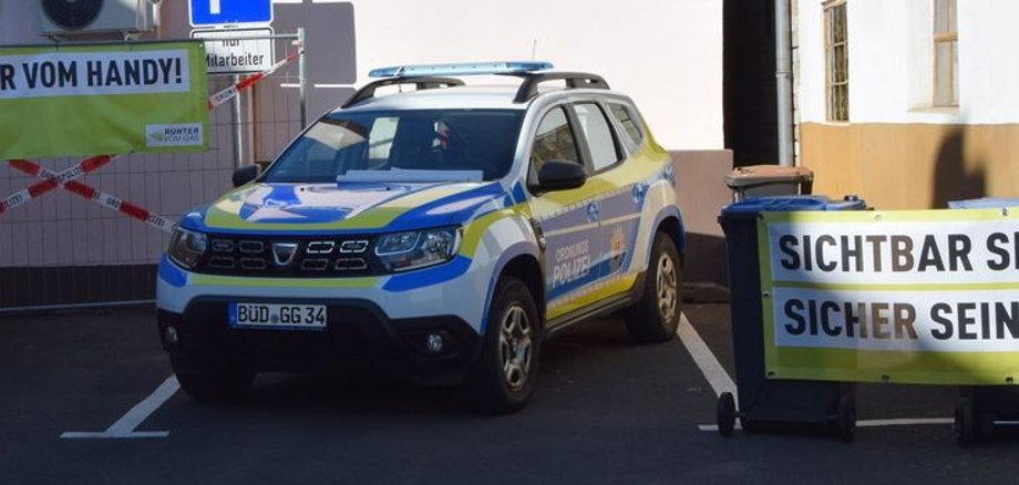 Ordnungsamt-KfZ Das Bild zeigt das KfZ des Ordnungsamtes auf dem Parkplatz. Links und rechts hängen Banner mit Ordnungsamtslogos "Sichtbar sein. Sicher sein." und "Finger vom Handy!"
