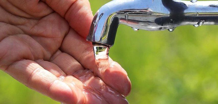 Hand und Wasserhahn aus einem Wasserhahn läuft Wasser in die geöffnete Hand