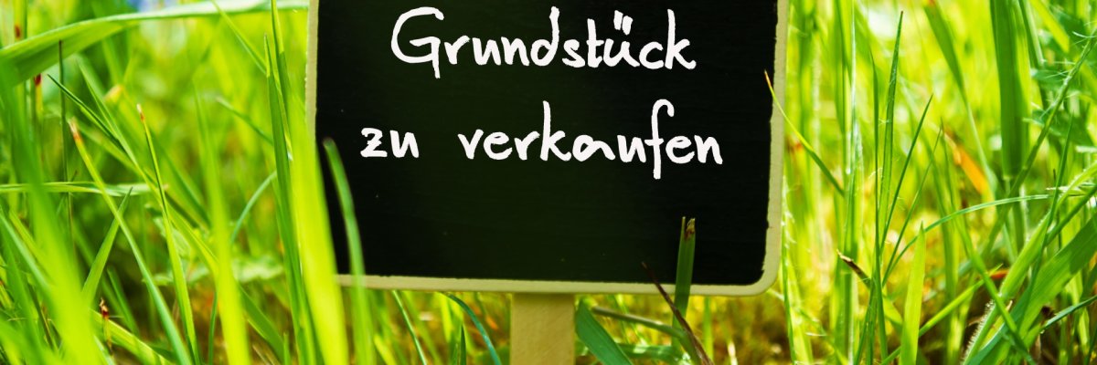 Wiese mit Schild Grüße Wiese, auf der ein Schild mit Grundstück zu verkaufen steht.
